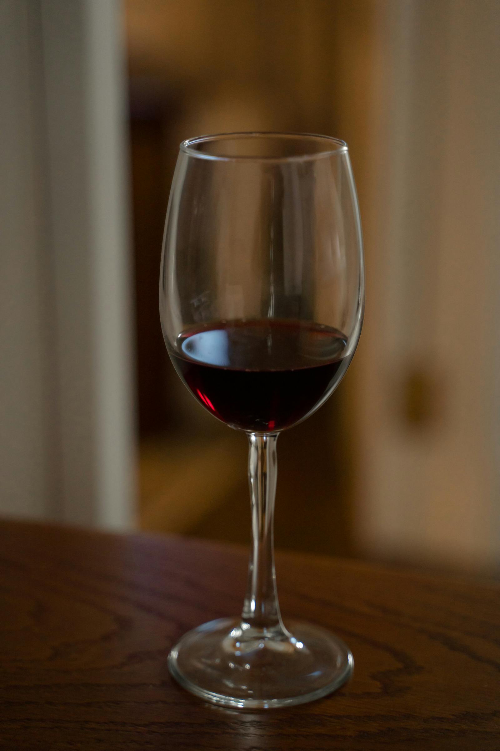 A glass of Vermora Estate Malbec, deep ruby-violet against the burgundy estate wall.